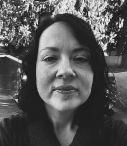 A black and white photo of a woman in front of trees.